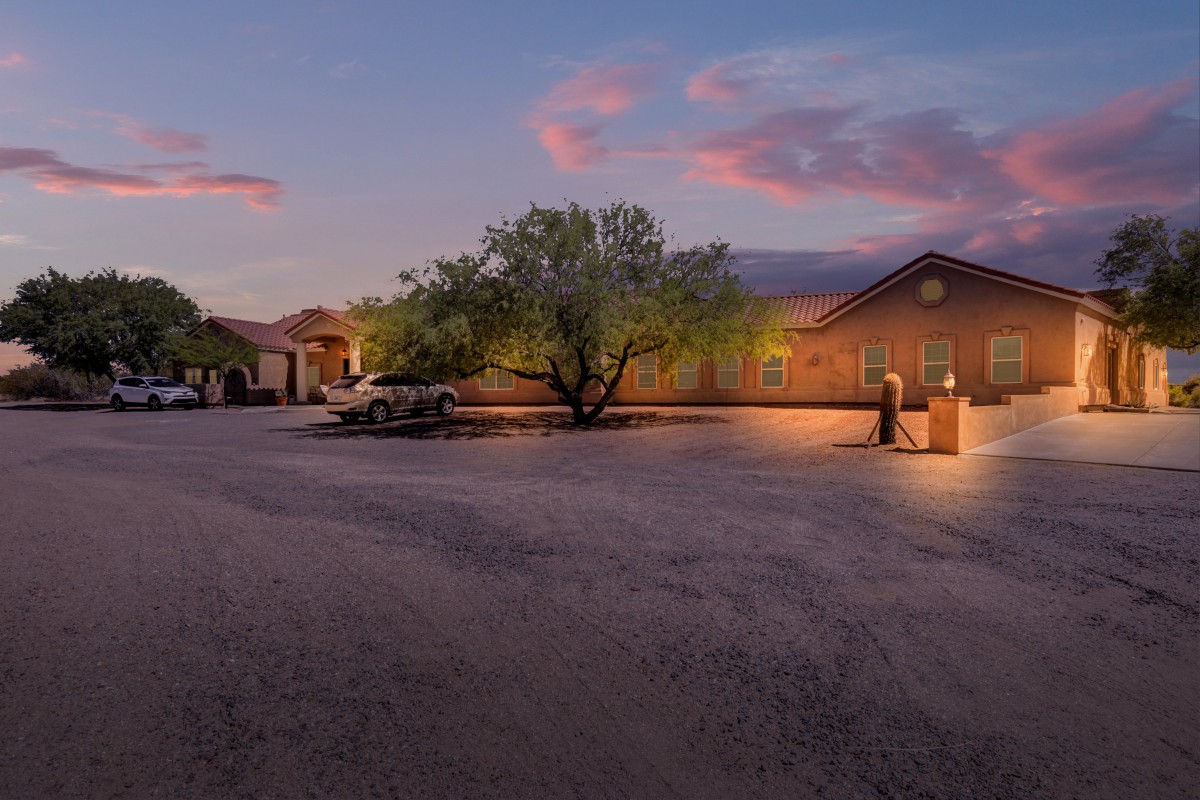 A serene parking lot at sunset with a large tree and a building in the background.