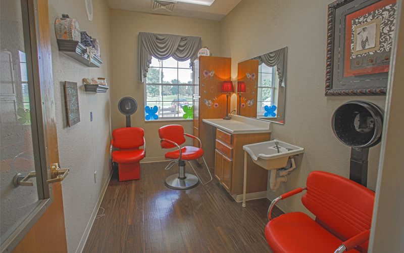 A cozy beauty salon interior with red chairs, a mirror, and a hair drying station.