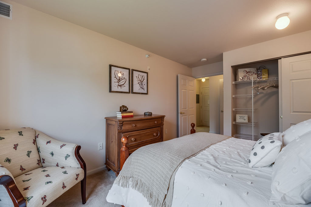 A cozy bedroom featuring a bed, dresser, and chair, with decorative artwork on the walls.