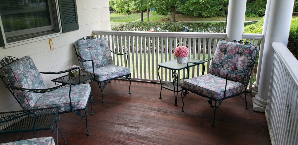 A cozy porch setup with cushioned chairs and a small table adorned with flowers.