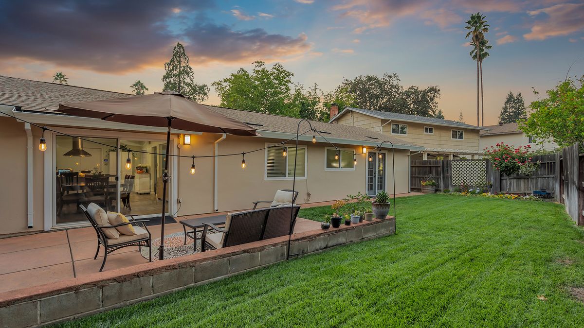 A cozy backyard with a well-maintained lawn and a patio featuring outdoor seating, surrounded by trees at sunset.