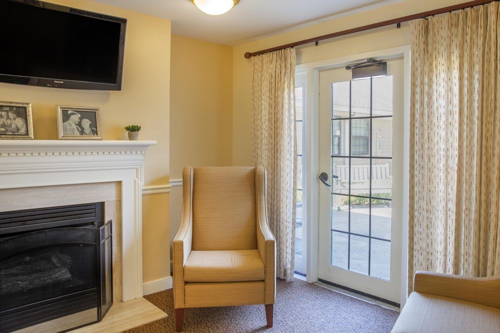 A cozy living room with a chair by the fireplace and a glass door leading outside.