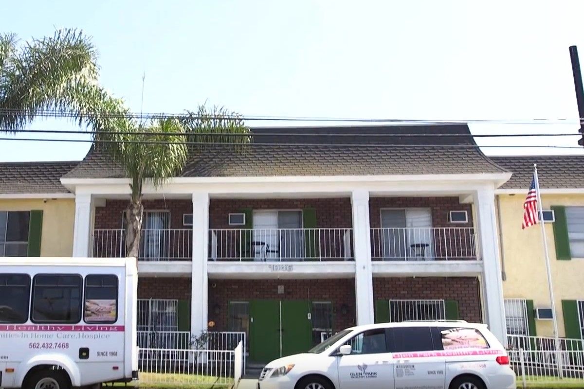 A two-story building with balconies and parked vehicles in front.