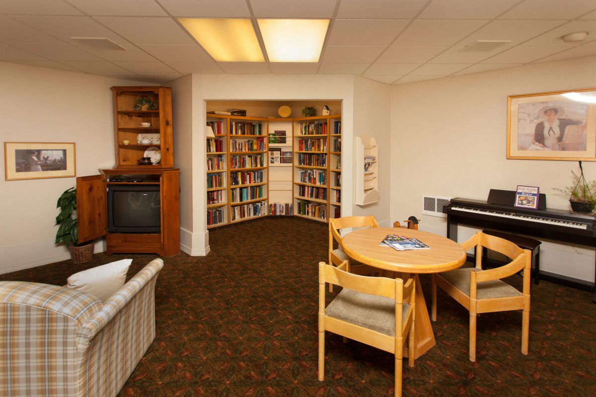 A cozy library room featuring bookshelves, a sofa, and a table with chairs.