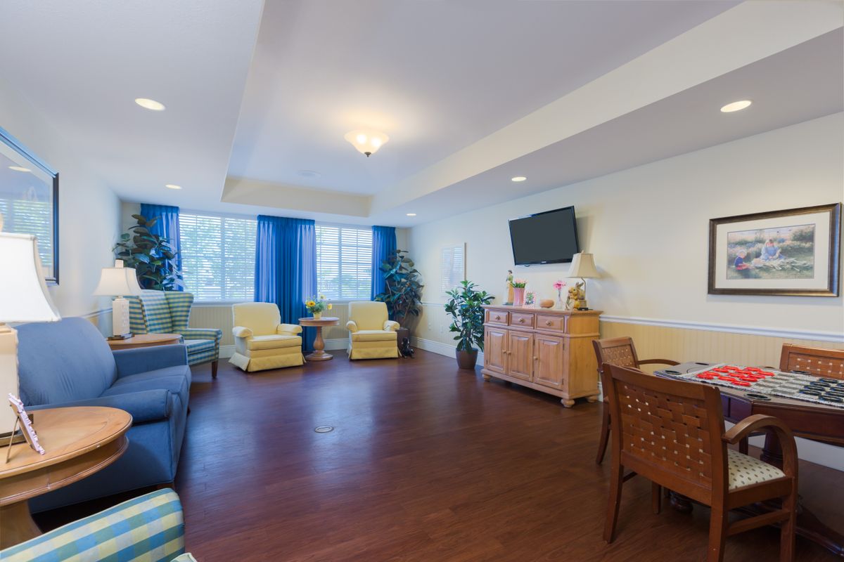 A spacious living room with comfortable seating, a television, and large windows with blue curtains.
