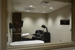 An interior view of a therapy or clinical room with a reclining chair and specialized lamp.
