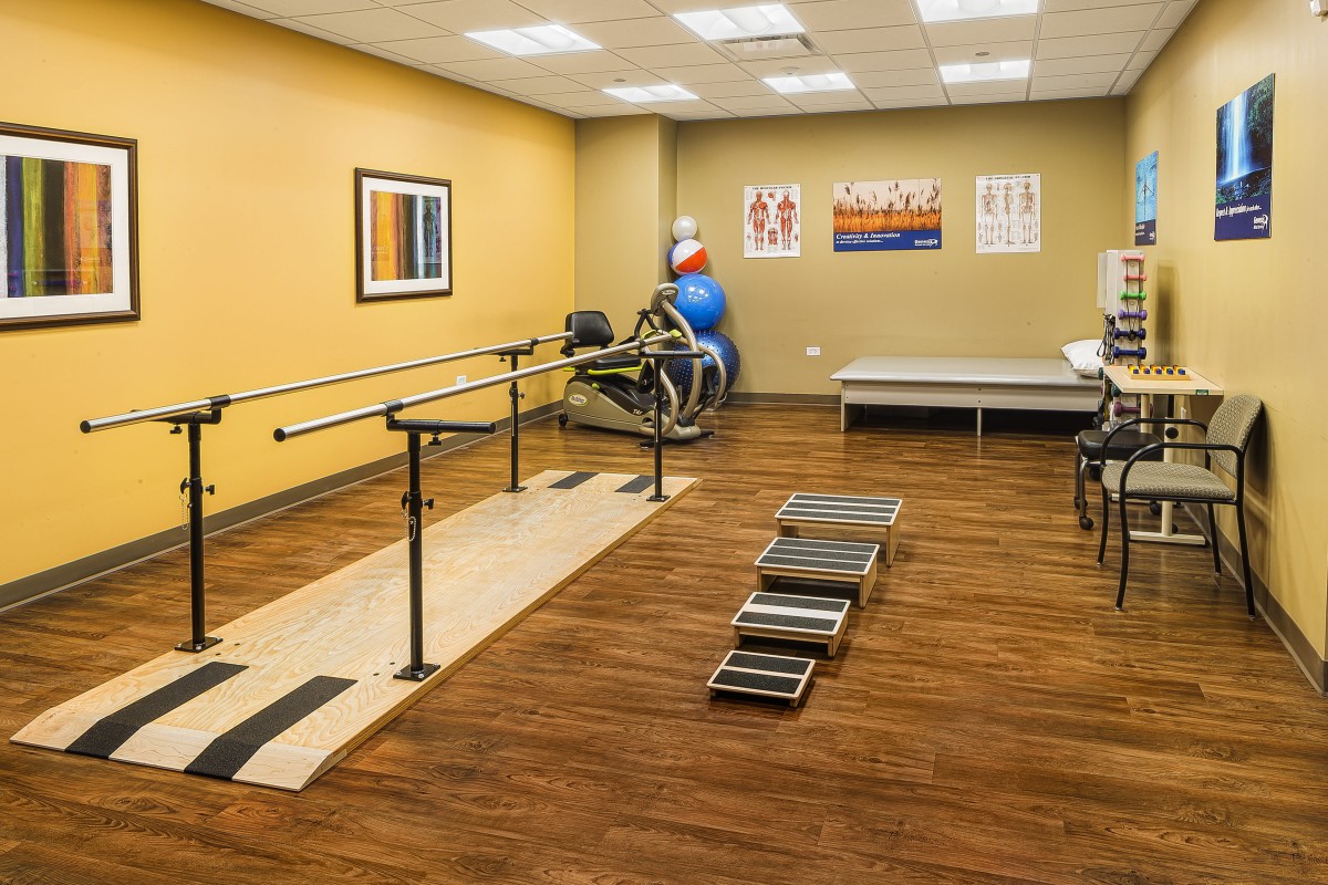 A well-equipped physical therapy room with exercise equipment and parallel bars.