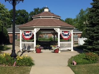 A gazebo decorated with red, white, and blue patriotic bunting, surrounded by flowers and a pathway.