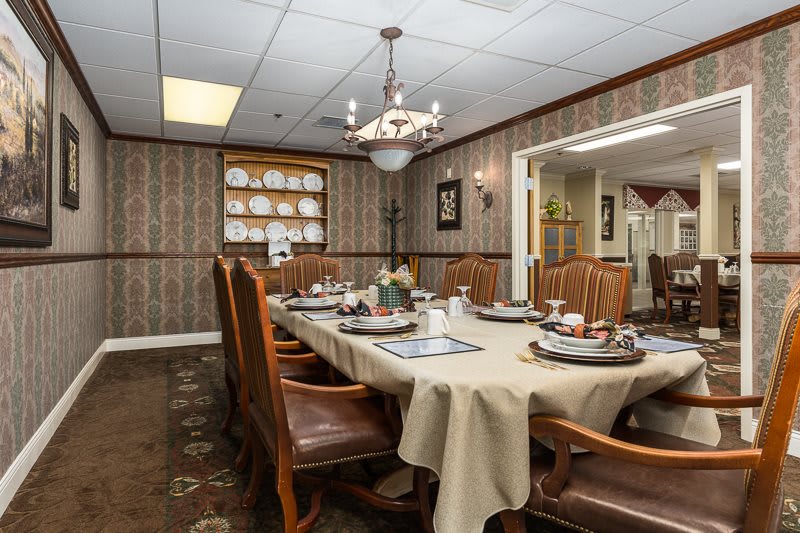 A traditional dining room with a set table, featuring elegant place settings and a central chandelier.