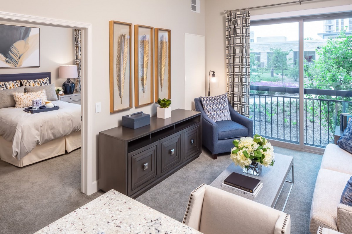 A modern living room with elegant furniture and decor, featuring a comfy armchair, decorative wall art, and a view of the outdoors.