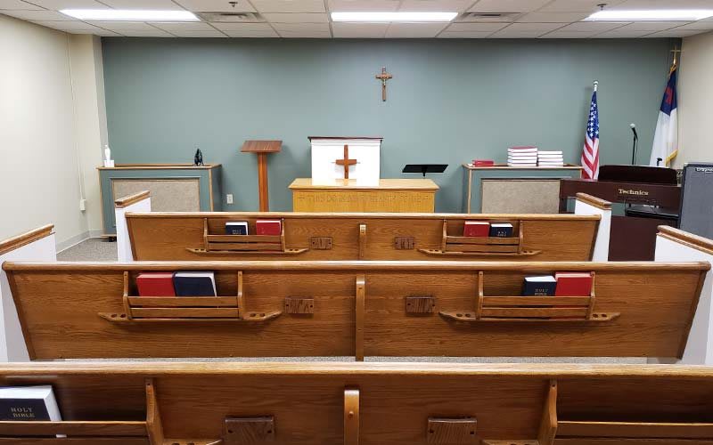 Interior of a small chapel with wooden pews facing an altar and a cross on the wall.