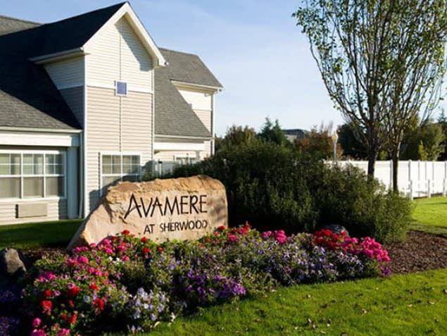 A landscaped garden with colorful flowers surrounds the sign for Awamere at Sherwood, next to a residential-style building.