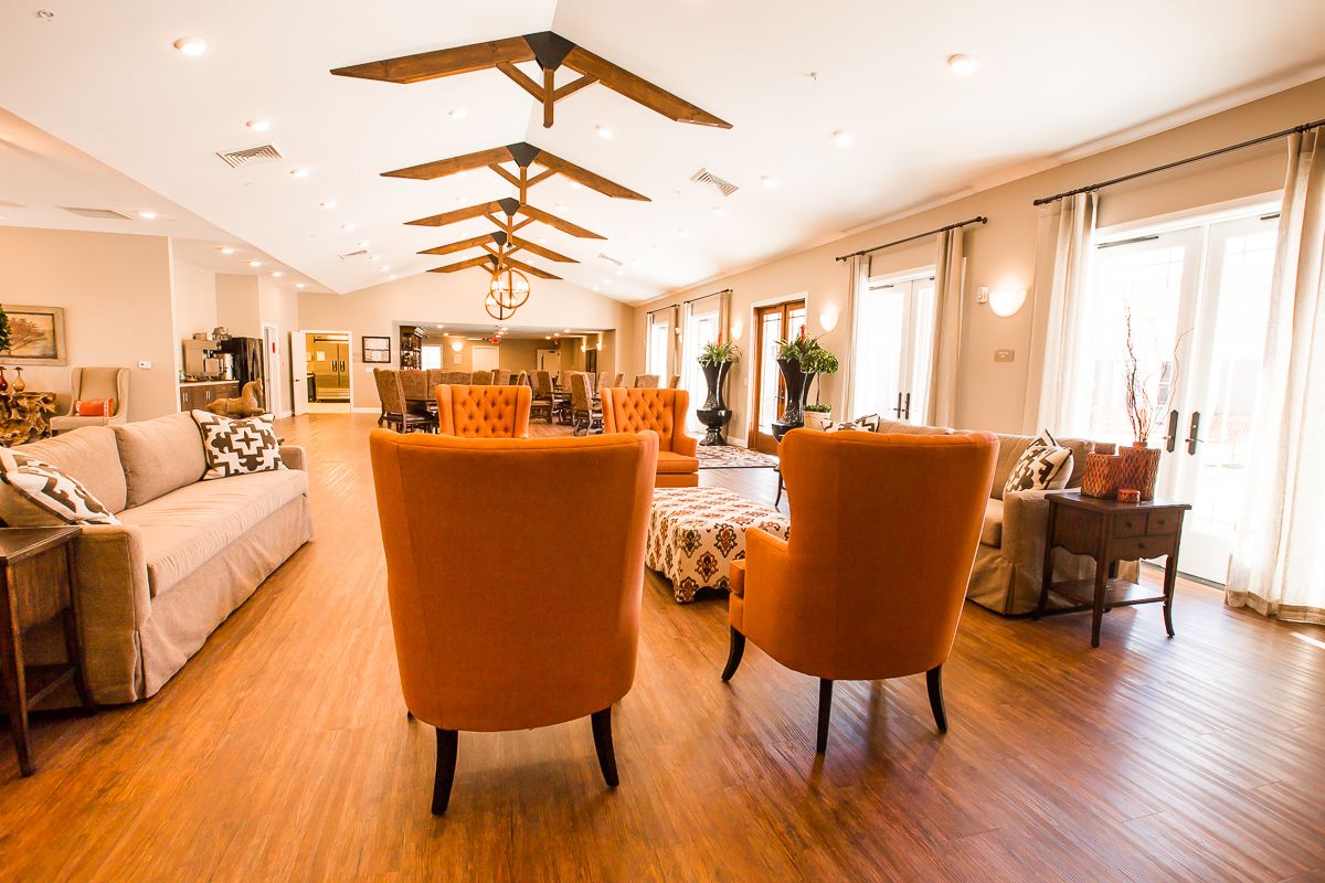 A spacious and well-lit lounge area with modern decor, featuring orange chairs and wooden flooring.