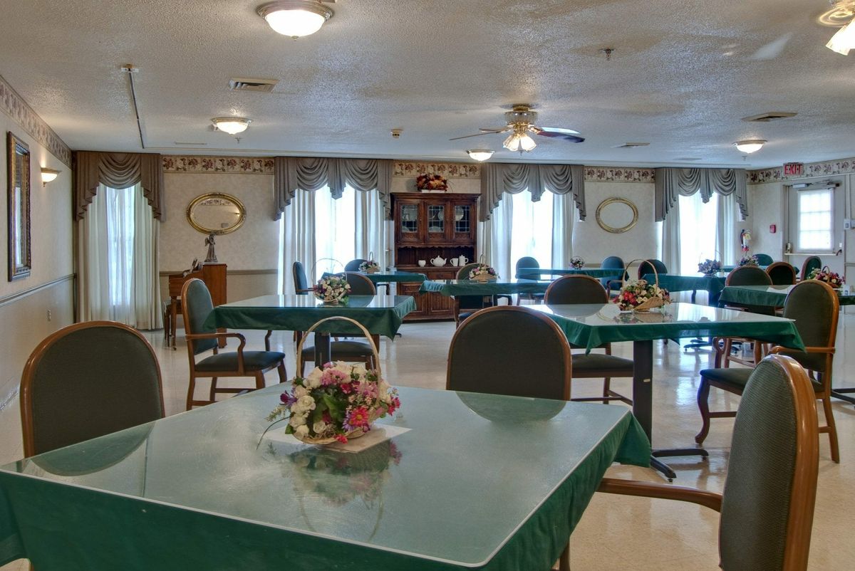 A well-lit dining room with green-covered tables and neatly arranged chairs.