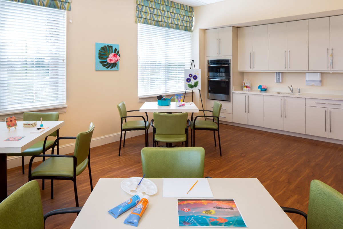 A bright art room with tables and chairs, featuring art supplies and a kitchen area.