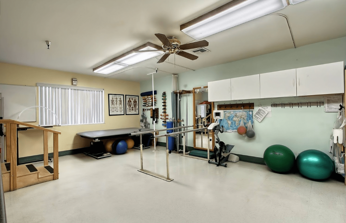A well-equipped physical therapy room with parallel bars, exercise balls, and a treatment table.