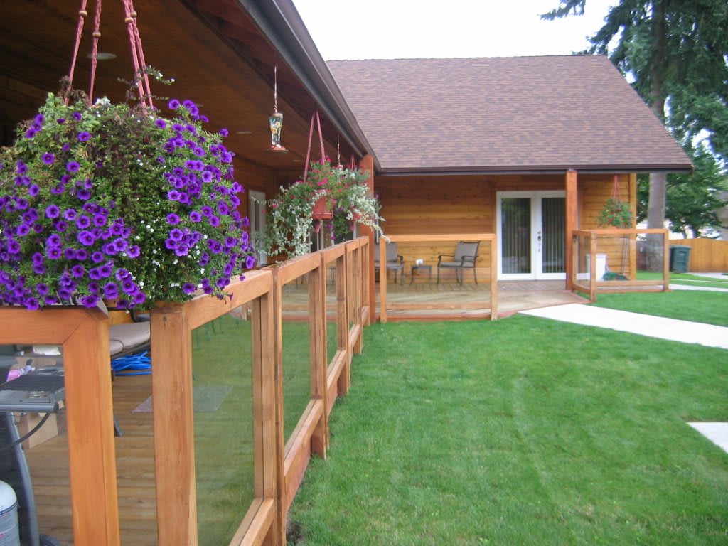 A cozy wooden house with a porch adorned with hanging flowers, overlooking a well-kept lawn and patio area.