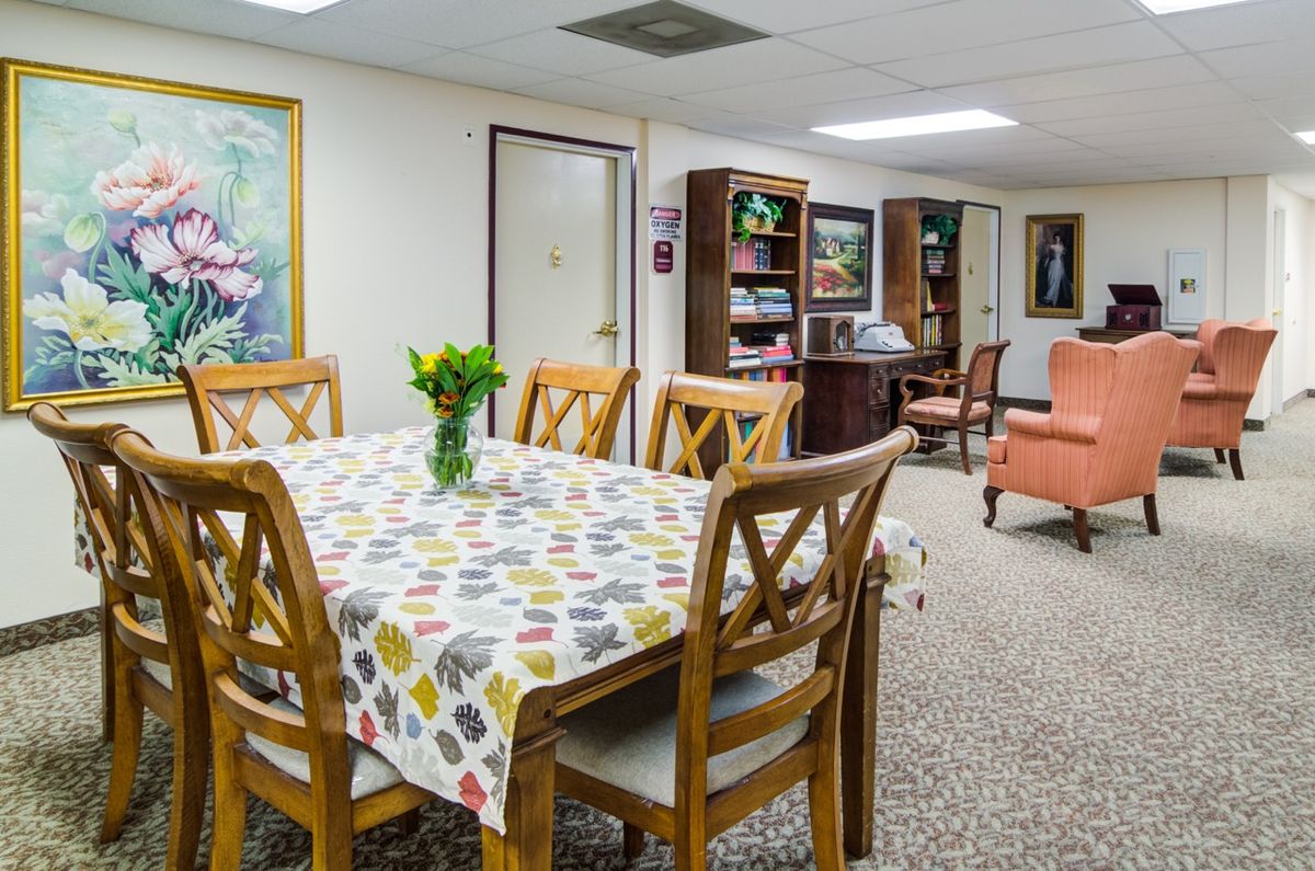 A cozy dining area with a table, chairs, and a bookshelf in a warmly decorated room.