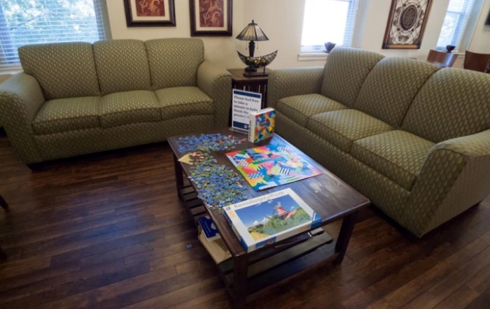 A cozy living room featuring green sofas, a wooden coffee table with puzzles, and decorative pieces.