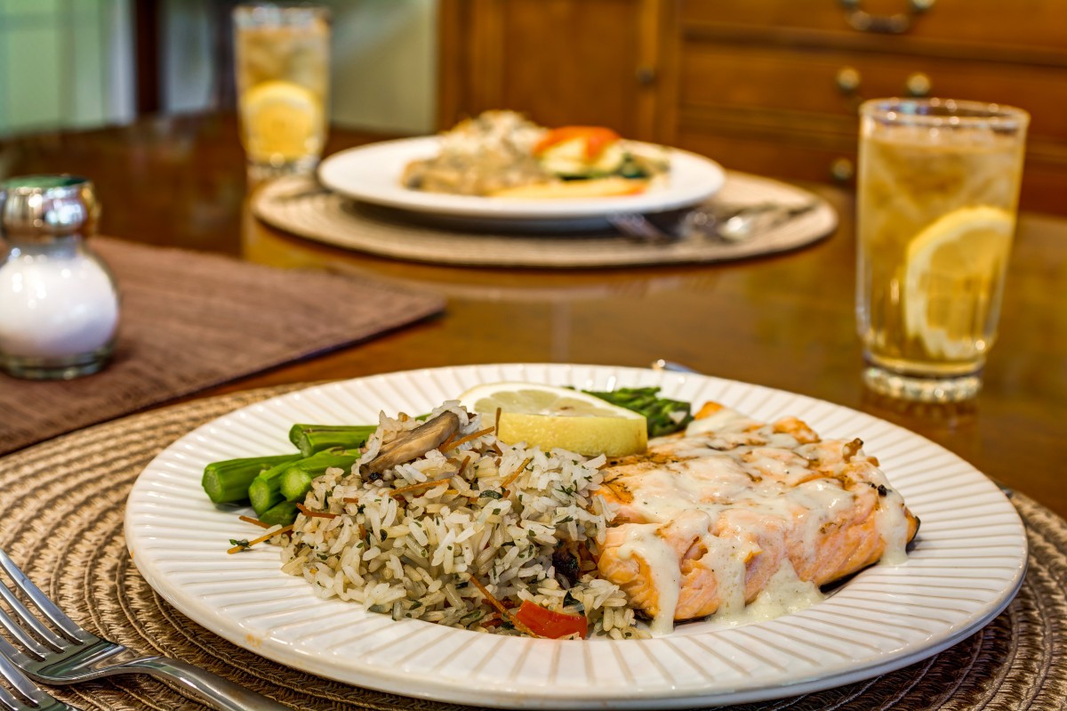 A dinner plate featuring salmon with a creamy sauce, served with wild rice and vegetables.