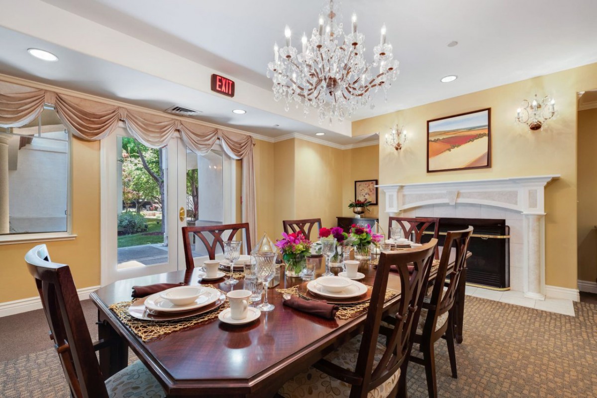 An elegant dining room with a beautifully set table, a chandelier overhead, and decorative elements including flowers and artwork.