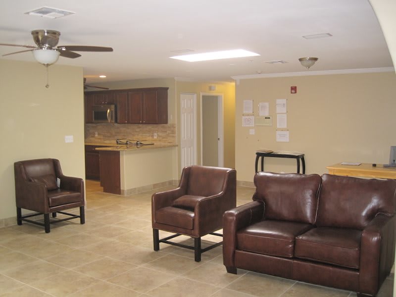 A spacious living area with leather chairs and couches, leading into a modern kitchen.