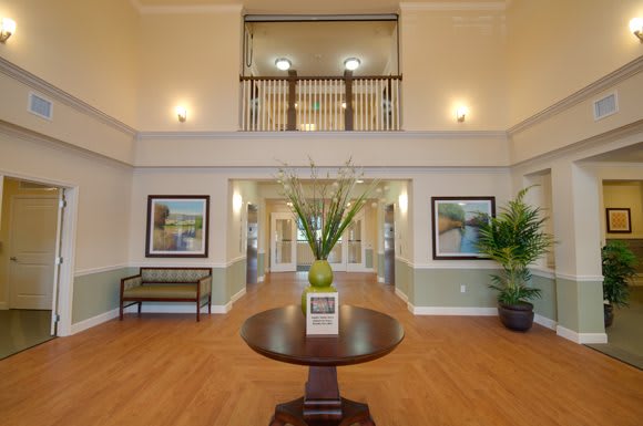 A spacious and elegant lobby featuring a central table with floral decor, framed artwork, and welcoming ambiance.