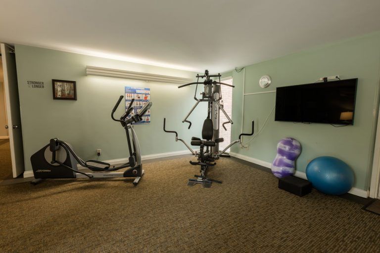 A home gym setup featuring an elliptical machine, a multi-gym station, and yoga accessories.