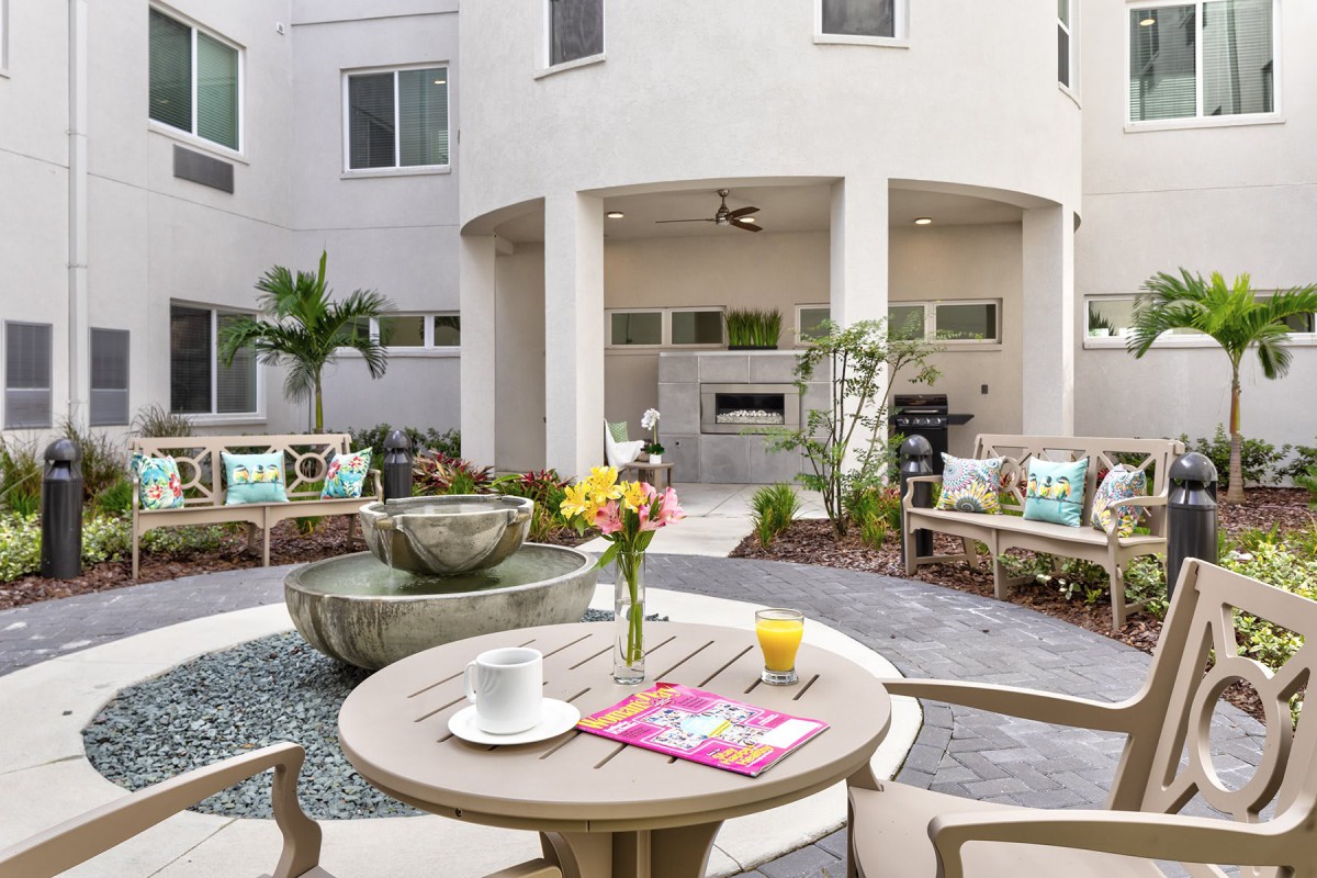 A serene outdoor patio featuring a central fountain, surrounded by cozy seating and a table set with flowers.