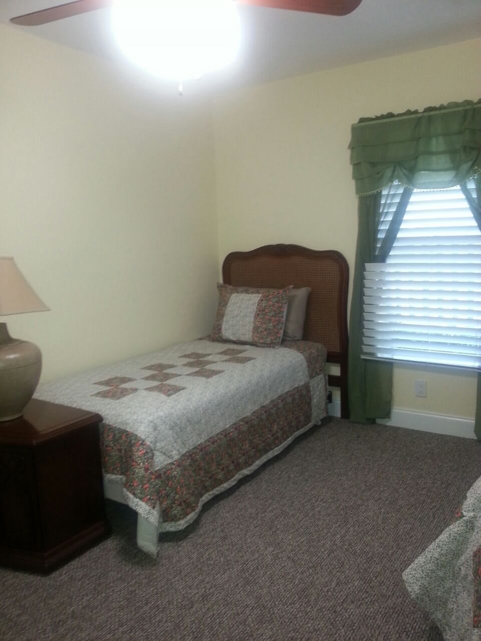 A cozy bedroom with a single bed and decorative quilt near a window with green curtains.