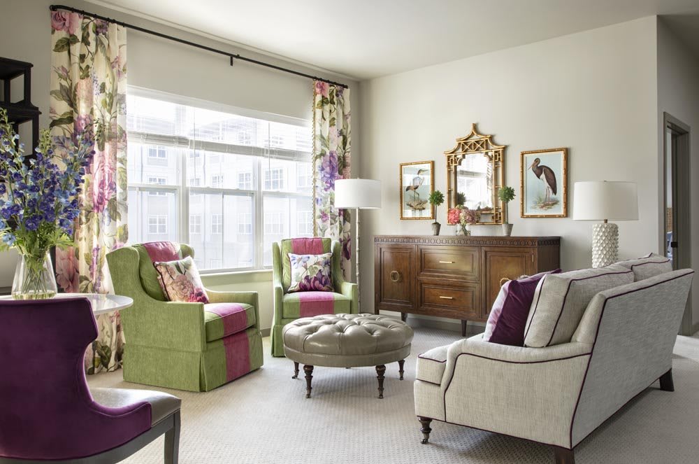 A cozy and elegantly decorated living room featuring colorful armchairs, a tufted ottoman, and wall art.