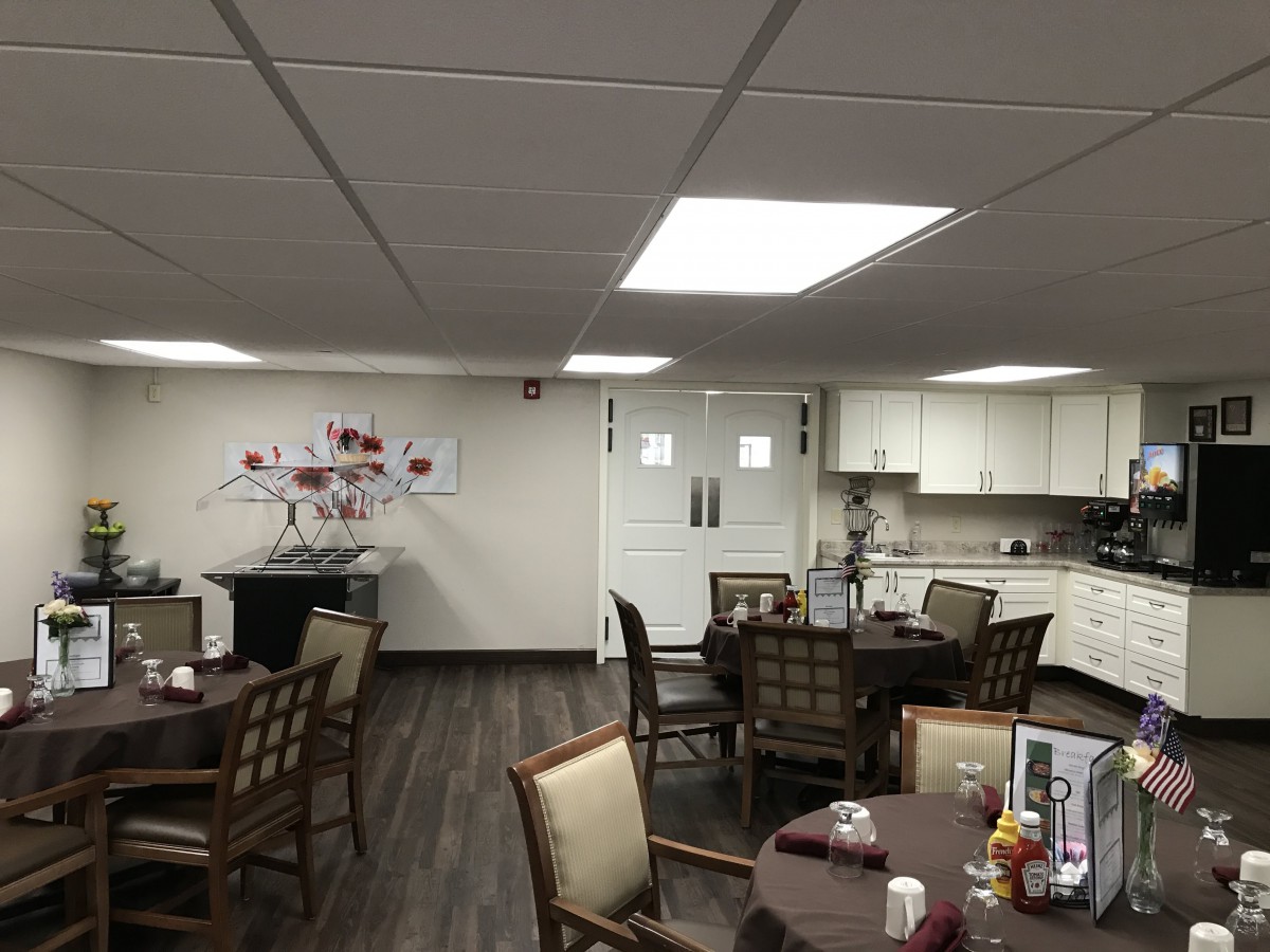 A cozy dining room with multiple tables and chairs, a small kitchen area, and decorative wall art.