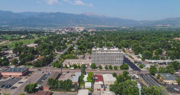 A scenic aerial view of a city with buildings surrounded by greenery and mountains in the background.