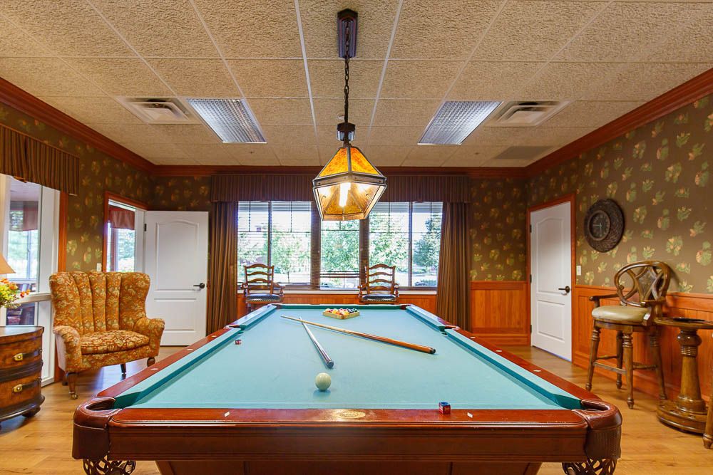 A cozy billiard room with a pool table and stylish interior design, featuring a hanging light and wood paneled walls.