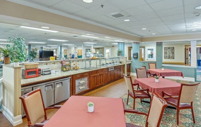 A spacious and well-lit dining area featuring neatly arranged tables and a buffet counter.