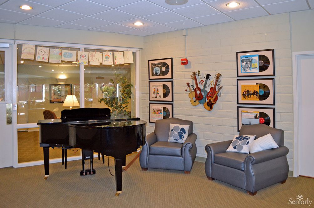 A cozy music room featuring a grand piano, comfy chairs, and musical-themed artwork on the walls.