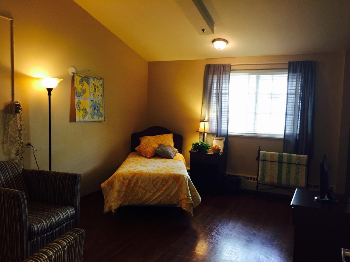 A cozy bedroom with a single bed, lamp, and window with curtains.