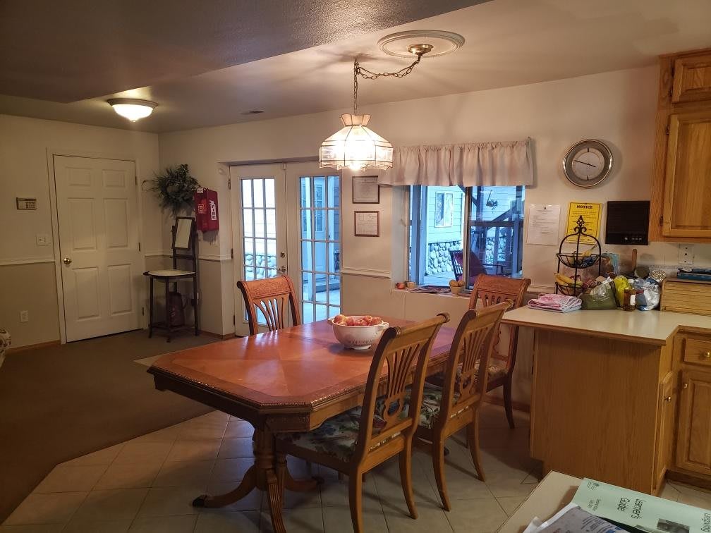 A cozy dining area with a wooden table and chairs, adjacent to a kitchen space, and well-lit by overhead lighting.