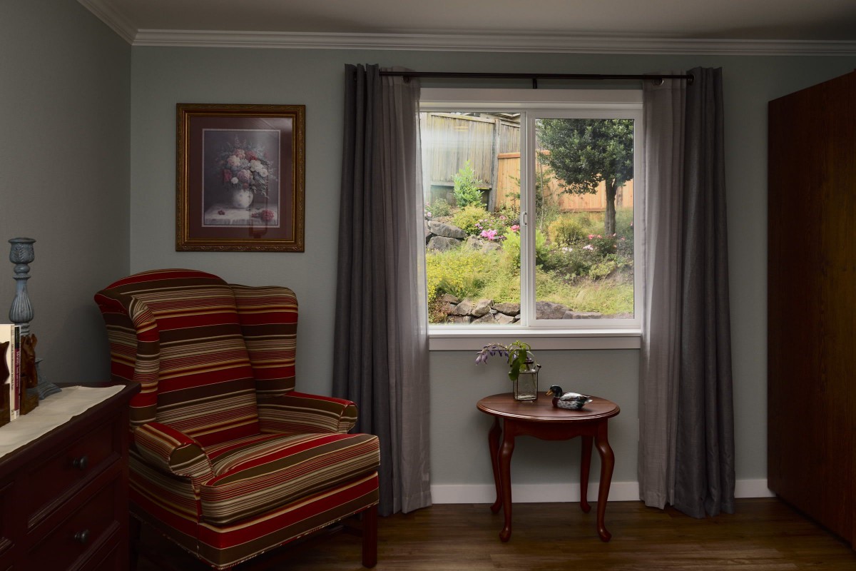A cozy living room with a striped armchair, small coffee table, and a view of a garden through the window.