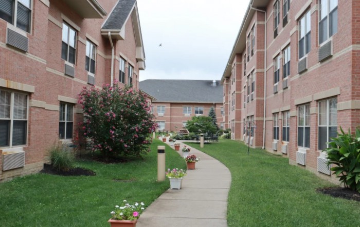 A well-maintained apartment complex with brick buildings, a landscaped sidewalk, and potted plants.