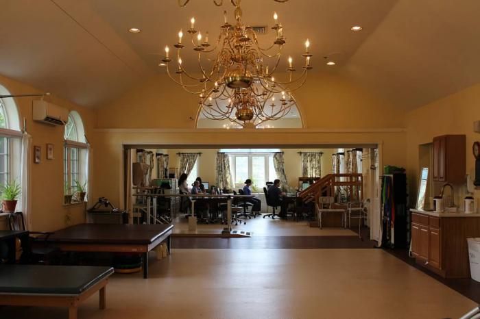 A spacious interior featuring a grand chandelier and mirrored walls, possibly a dance studio.