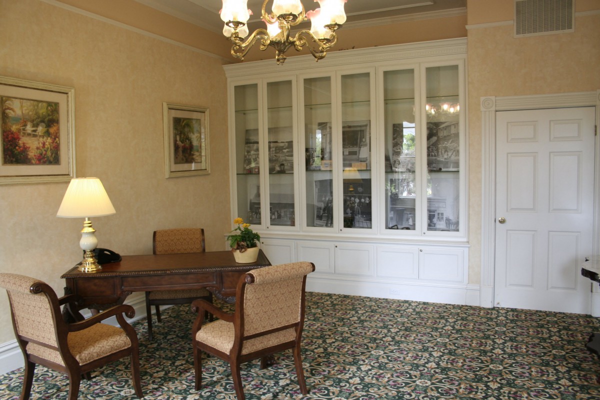 A traditional living room with a wooden desk, chairs, built-in cabinet, and a decorative carpet.