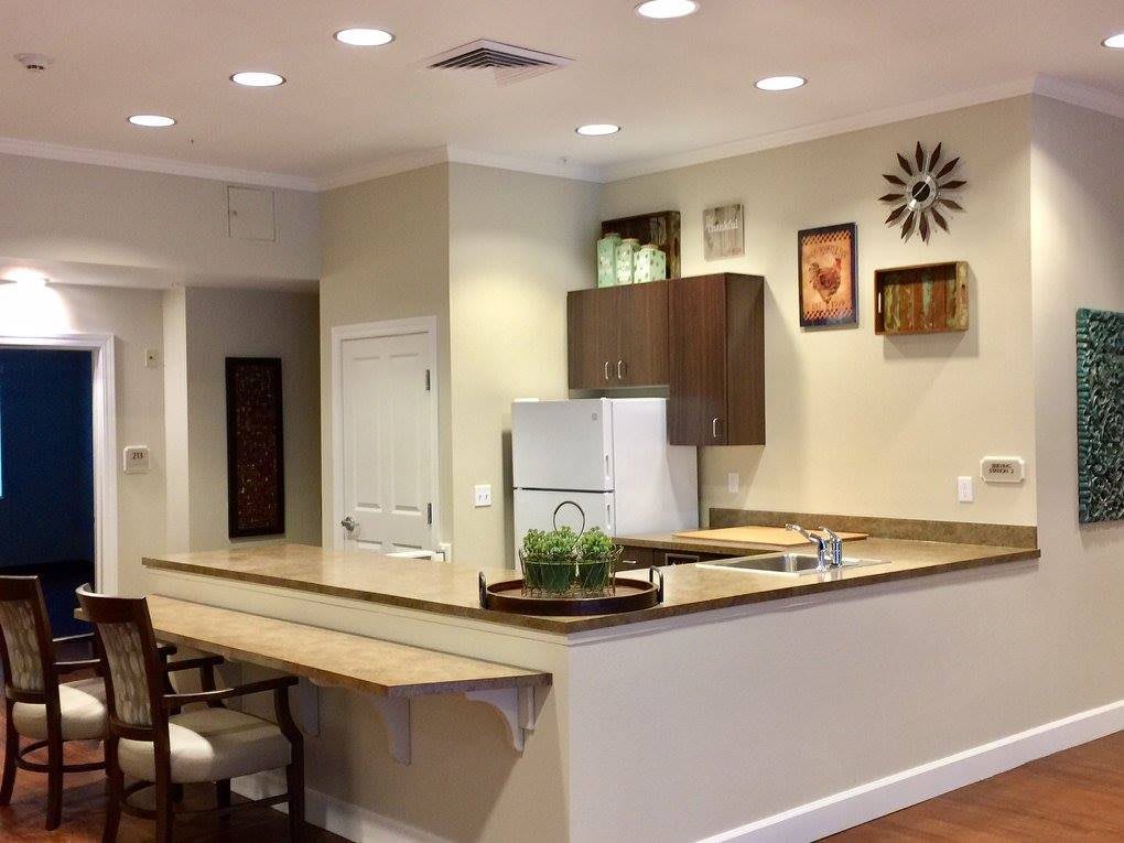 A modern kitchen featuring a countertop with decorative items, white appliances, wall-mounted artwork, and recessed lighting.