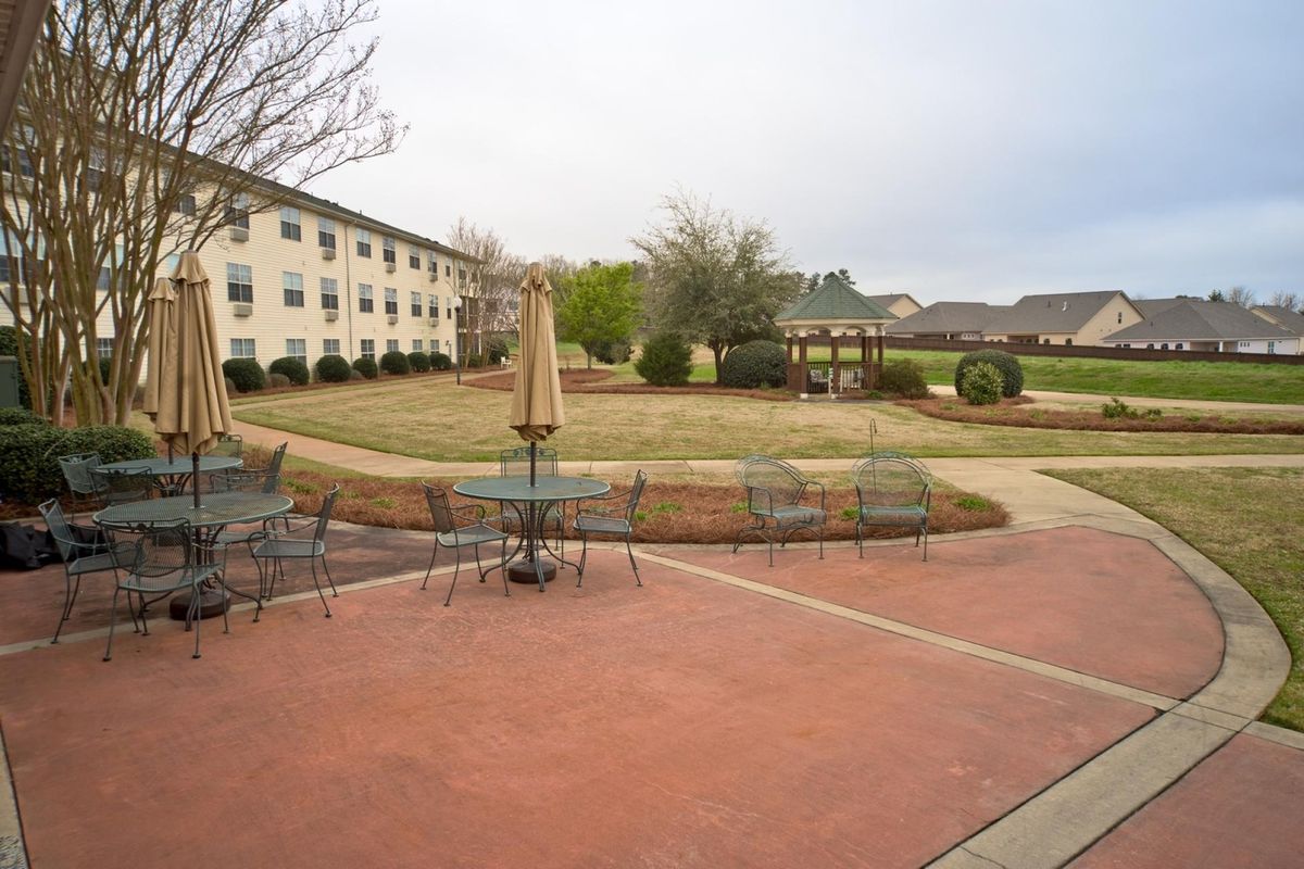 A courtyard with outdoor seating, surrounded by a pathway and trees, adjacent to a residential building.