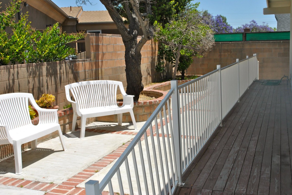 A sunny patio area with white furniture and a fenced garden.