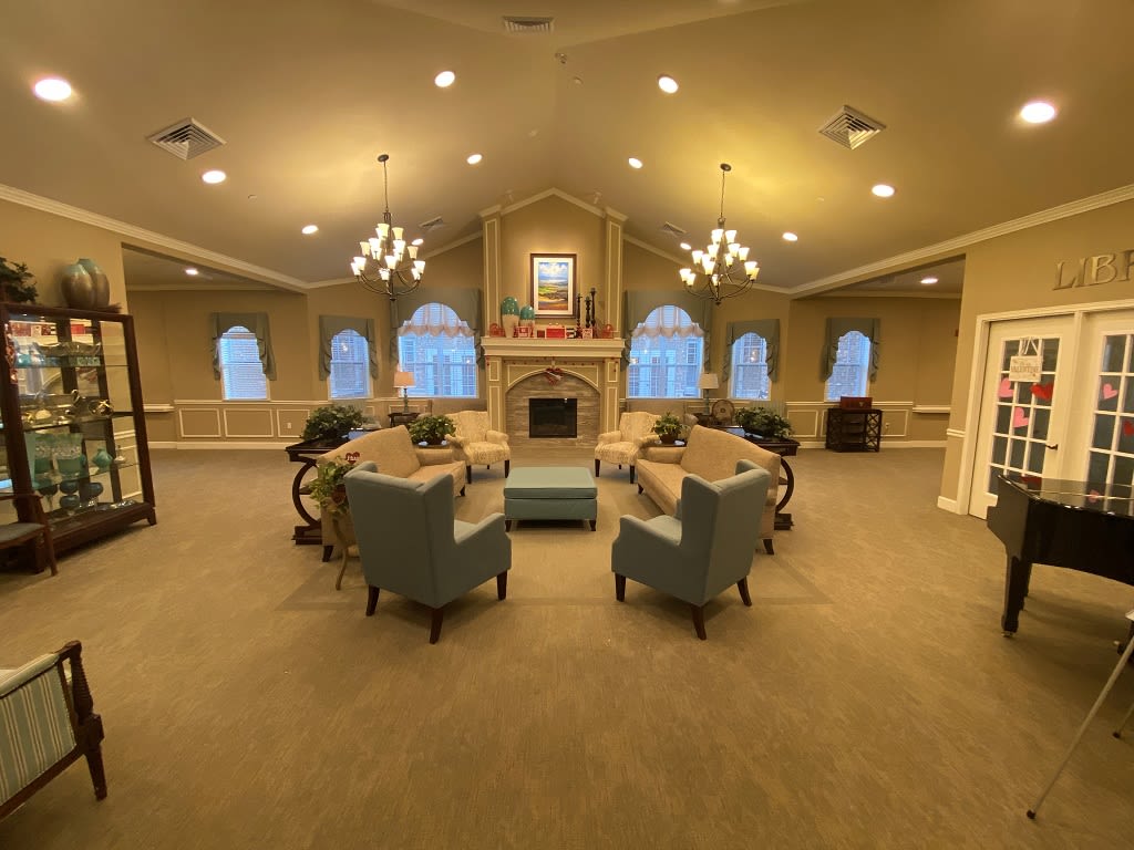 A spacious and elegantly decorated living room with chandeliers, a central fireplace, and comfortable seating arrangement.