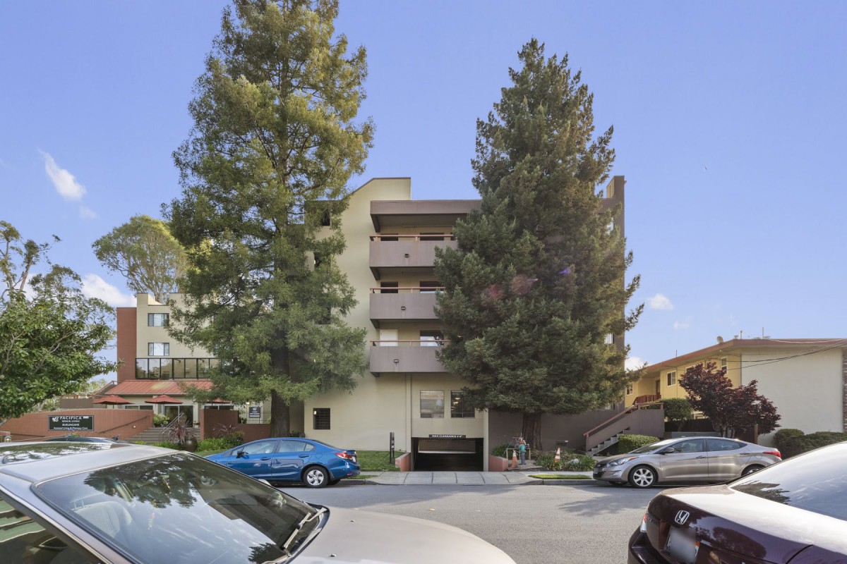 A residential building with large trees and parked cars in front.