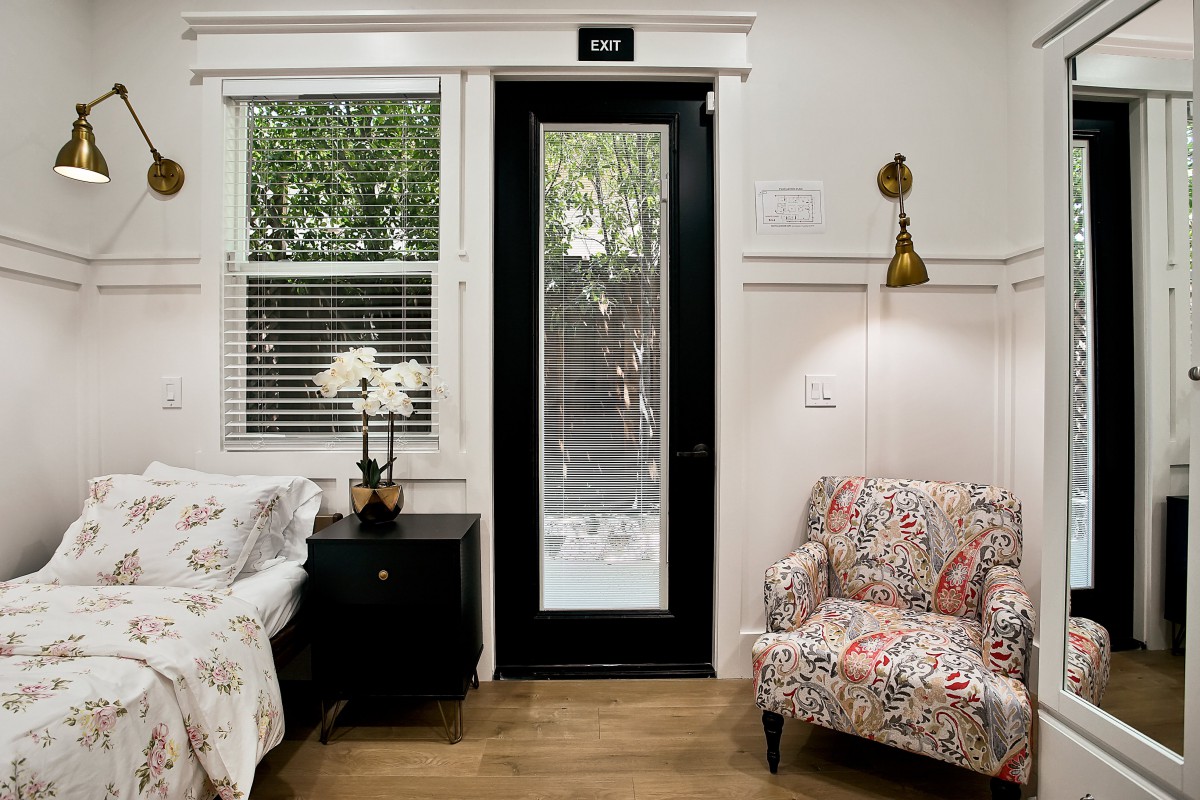 A cozy living room featuring a black-framed glass door with an exit sign, surrounded by a floral armchair, sofa, and decorative elements.