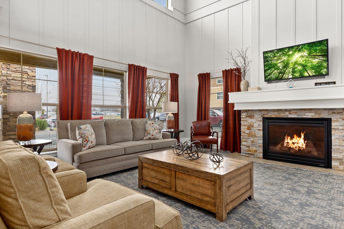 A cozy living room with a sofa, fireplace, and large windows adorned with red curtains.