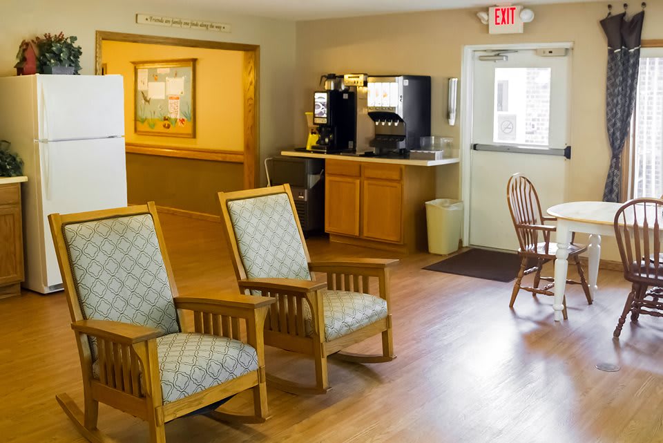 A cozy indoor waiting area with wooden chairs, a coffee machine, and wooden flooring.